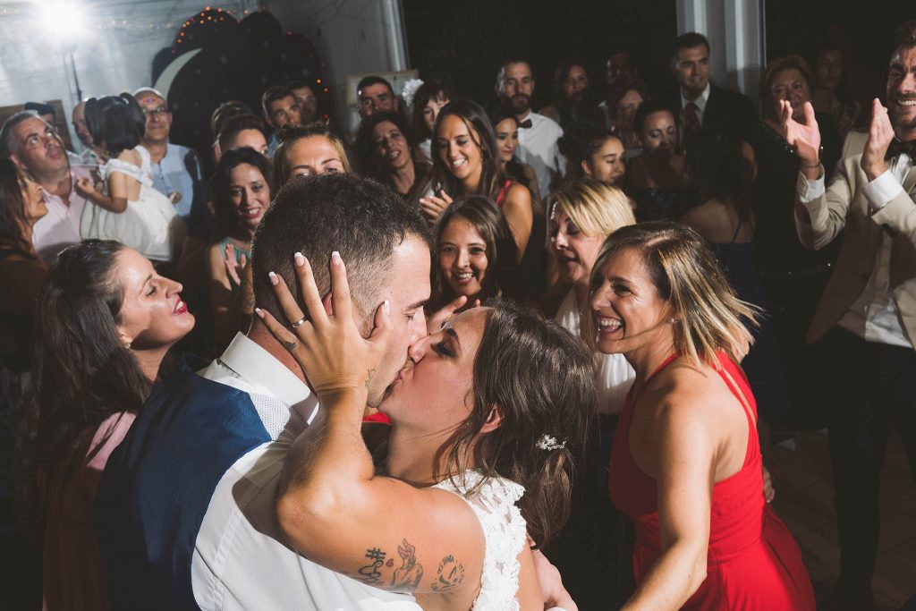 Los novios dándose un beso durante la fiesta el día de la boda, entre sus invitados